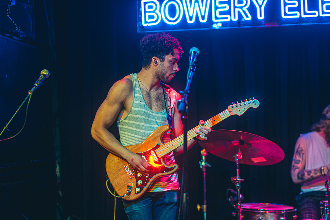 A man in a tank top plays electric guitar on stage